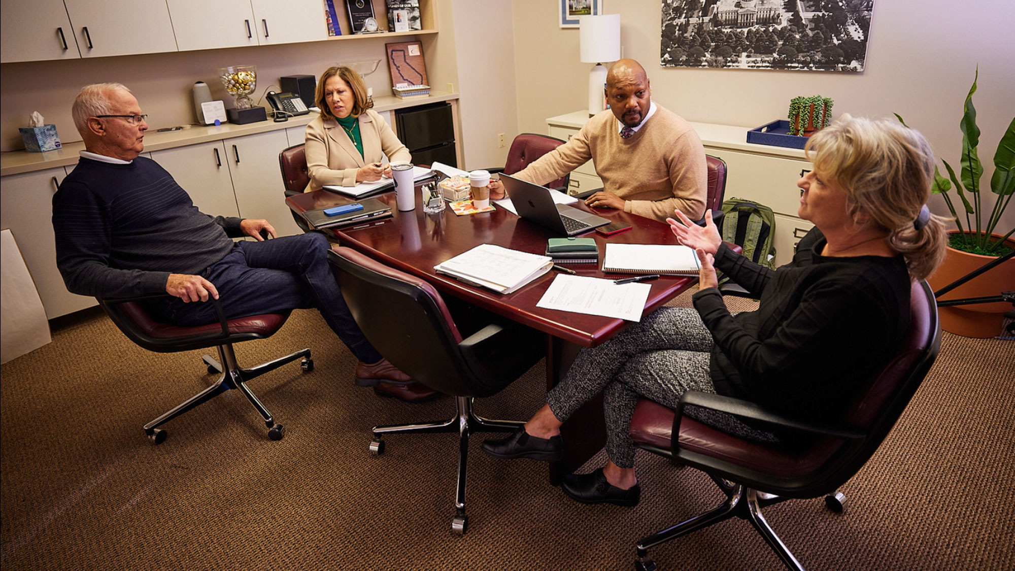 Positioned clockwise, seated around a conference table, Jeff Frost, Andrea Ball, Khieem Jackson, and Laura Wasco meet with each other. Laura is talks to the group and gestures with her hands.